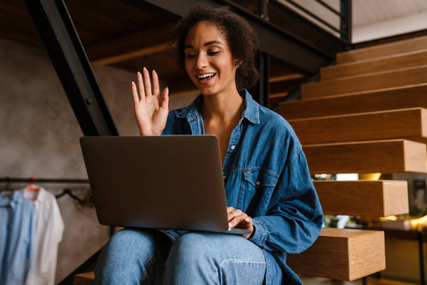 Young black woman wearing denim shirt smiling and using laptop at home - Foto, imagen