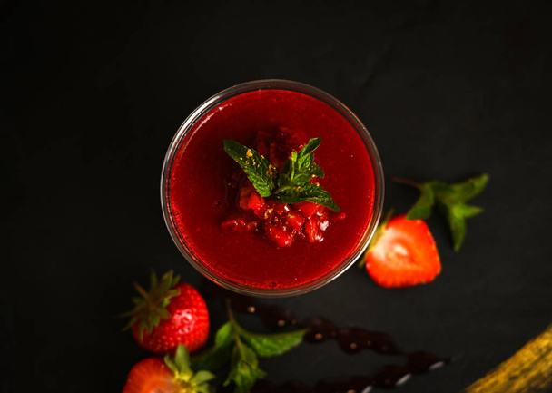 Glass of tasty strawberry smoothie on the dark background, decorated with mint and berries - Foto, immagini