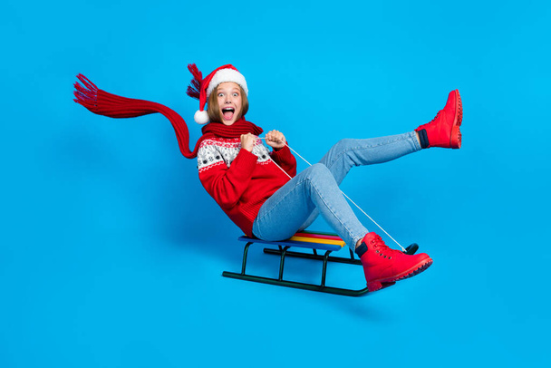 Full length photo of excited funky school girl dressed red x-mas ornament pullover enjoying sledges isolated blue color background. - Фото, изображение