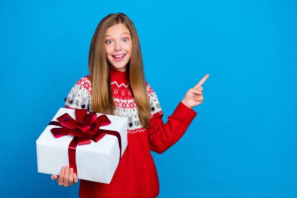 Photo of impressed girl with straight hairstyle dressed red pullover hold present directing empty space isolated on blue color background. - Foto, Imagem