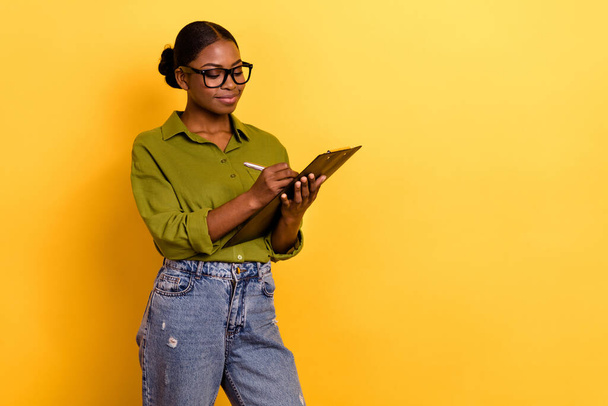 Portrait of attractive focused skilled cheerful girl writing note plan list copy space isolated over bright yellow color background. - Fotó, kép