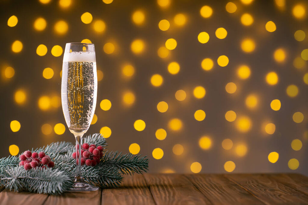 Wine glass with bubbly champagne and fir branch with decor on background of blurry sparkling lights. Happy New Year holiday greeting card, banner, header with copy space - Photo, Image