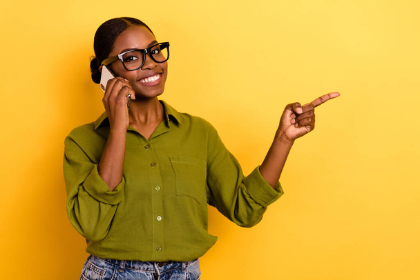 Portrait of beautiful trendy cheerful girl calling friend talking showing copy space isolated over bright yellow color background. - Фото, изображение