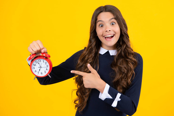 Excited face. Portrait of teenage girl with clock alrm, time and deadline. Studio shot isolated on yellow background. Amazed expression, cheerful and glad - Foto, afbeelding