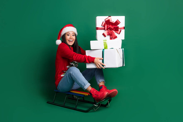 Full length photo of pretty surprised lady wear red ugly print xmas sweater sledding rising presents stack pile isolated green color background. - Fotó, kép