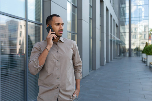 Worried and upset young Spanish man. African-American man stands on the street, talks on the phone, looks away. - 写真・画像