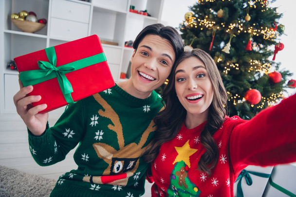 Portrait of two cheerful overjoyed people take selfie hold showing newyear desirable giftbox indoors. - Foto, immagini