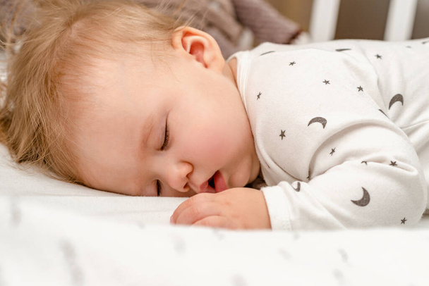 Nahaufnahme Porträt eines blonden Babys, das ruhig auf seinem Bauch in einem Kinderbett schläft. - Foto, Bild