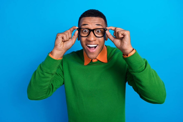 Portrait of positive cheerful overjoyed guy orange shirt under green pullover fingers touching glasses isolated on blue color background. - Φωτογραφία, εικόνα