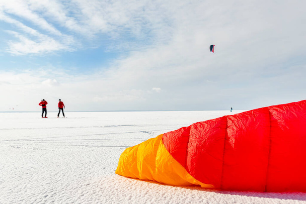 Panoramic view of many people frineds enjoy riding kite surf board in warm suit on bright sunny winter day at frozen lake field snowy surface. Wintersport adrenaline fun adventure hobby acitivity. - Photo, Image