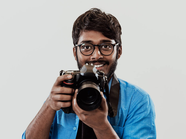 Professional photographer having DSLR camera taking picture.Indian man photography enthusiast taking photo while standing on blue background. Studio shot.  - Фото, зображення