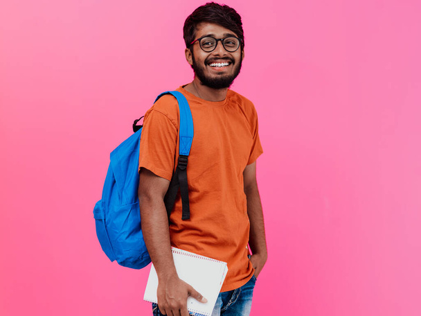  Indian student with blue backpack, glasses, and notebook posing on pink background. The concept of education and schooling. Time to go back to school.  - Foto, Imagem