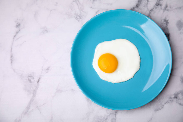 Tasty fried egg in plate on white marble table, top view. Space for text - Foto, imagen
