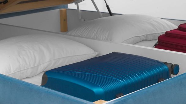 Storage drawer under bed with blue suitcase and white pillows indoors, closeup - 写真・画像