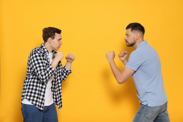 Two emotional men fighting on yellow background - Фото, зображення