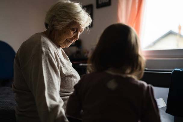 Idős nő idős kaukázusi nyugdíjas idős nagymama kislánnyal gyermek kisgyermek töltenek időt együtt otthon könyvek gondozása és a családi koncepció generációs támogatás együtt valós emberek - Fotó, kép
