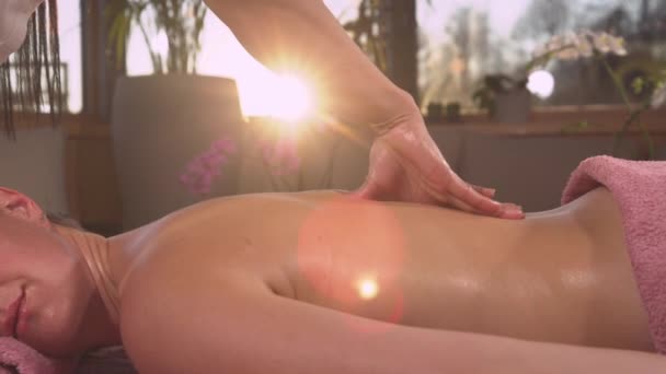 CLOSE UP: Während der Rückenmassage scheint goldenes Sonnenlicht durch weibliche Hände. Detaillierte Ansicht der arbeitenden Hände der jungen Frau bei der Körpermassage. Entspannende Wellness-Behandlung am Ende des Tages - Filmmaterial, Video