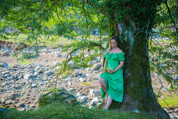 с цветами в зеленом платье, девушка стоит у дерева. Высокое качество фото - Фото, изображение