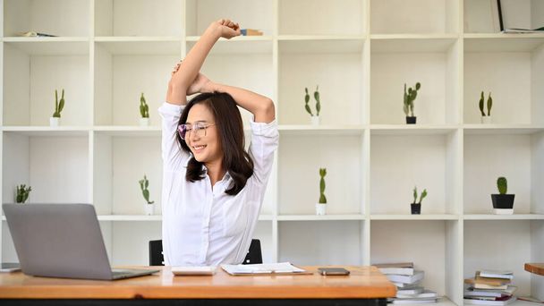 美しい若いアジアの実業家や女性のオフィスの従業員は、仕事の後にリラックスし、彼女の腕を伸ばし、彼女のオフィスで休んで. - 写真・画像