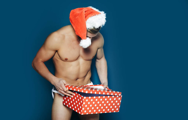 Christmas sexy man. Young men in santa hat. New year. Muscle man at xmas. Santa with muscular body. Christmas party and sex games. Handsome sexy santa claus guy on blue background - Foto, Imagen