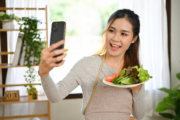 Nádherná a okouzlující mladá asijská žena nebo žena v domácnosti pomocí svého smartphonu vyfotit sebe a její domácí salát v kuchyni. Zdravý životní styl koncept  - Fotografie, Obrázek