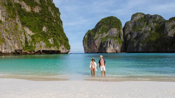 Taylandlı kadınlar ve beyaz erkekler kumsalda yürürler ve kameraya bakarlar, Maya Körfezi sahili Koh Phi Phi Tayland Sabahları turkuaz renkli okyanuslarla.  - Fotoğraf, Görsel