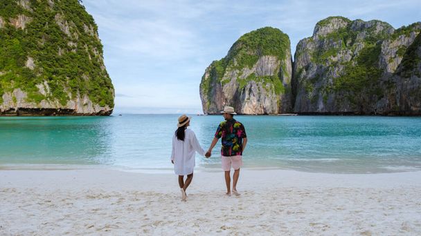 Taylandlı kadınlar ve beyaz erkekler Maya Körfezi plajında yürüyorlar Koh Phi Phi Tayland 'da turkuaz renkli okyanuslarla.  - Fotoğraf, Görsel