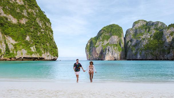 Taylandlı kadınlar ve beyaz erkekler sabahları turkuaz renkli okyanuslarla Maya Körfezi sahilinde Koh Phi Phi Tayland 'da yürürler..  - Fotoğraf, Görsel