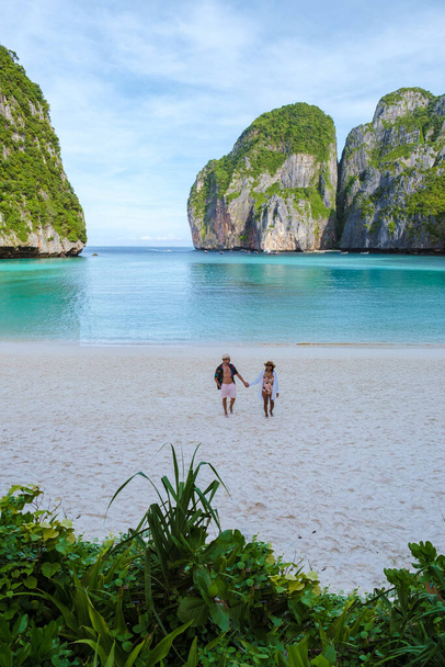 Couple walking on a empty beach, Thai women and caucasian men walk on the beach of Maya Bay beach Koh Phi Phi Thailand in the morning with turqouse colored ocean.  - Photo, Image