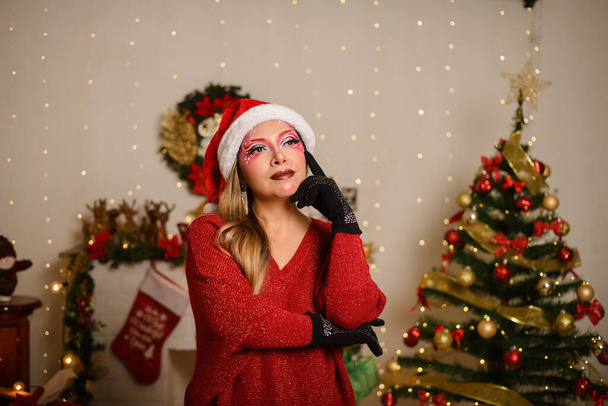 Junge Frau mit weihnachtlichem Fantasie-Make-up in nachdenklicher Haltung. Weihnachtlicher Hintergrund. - Foto, Bild