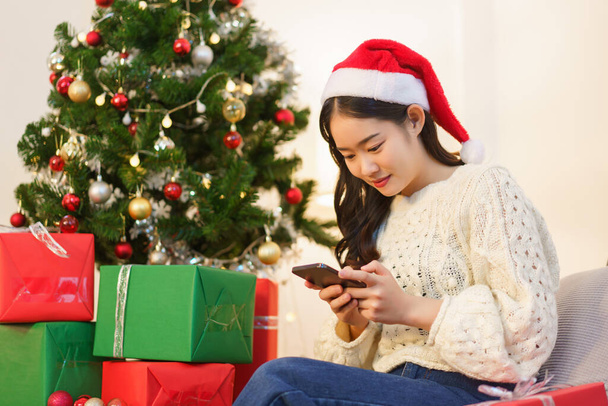 Conceito de Natal, mulher asiática senta-se na sala de estar decorada de Natal e conversando no smartphone. - Foto, Imagem