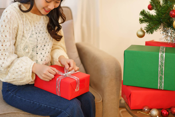 Noel konsepti, Asyalı bir kadın Noel süslemeli oturma odasında oturuyor ve Noel hediyesini açıyor.. - Fotoğraf, Görsel