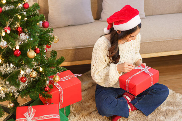 クリスマスのお祝いのコンセプト、若いアジアの女性が床に座ってクリスマスプレゼントを開く. - 写真・画像