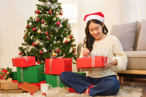 クリスマスのコンセプト、アジアの女性はクリスマスの装飾されたリビングルームとオープンクリスマスプレゼントに座って. - 写真・画像