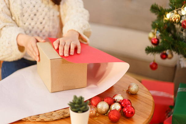 Christmas concept, Young asian woman in santa hat using red paper to wrapping christmas gift box. - Photo, Image