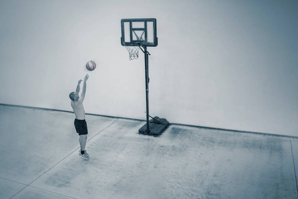 Aerial view of Caucasian man throwing a basketball into a hoop while practicing in the court - Фото, зображення