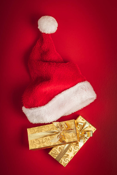 Gold christmas gift and red Santa hat on the red background. Top view. - Fotoğraf, Görsel