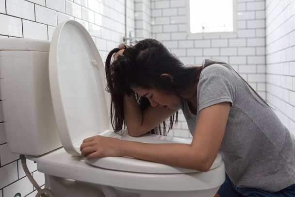 Woman drunk hangover puke in toilet bowl. Female have abdominal pain, nausea, dizziness, nausea, vomit due to food poisoning. - Photo, Image