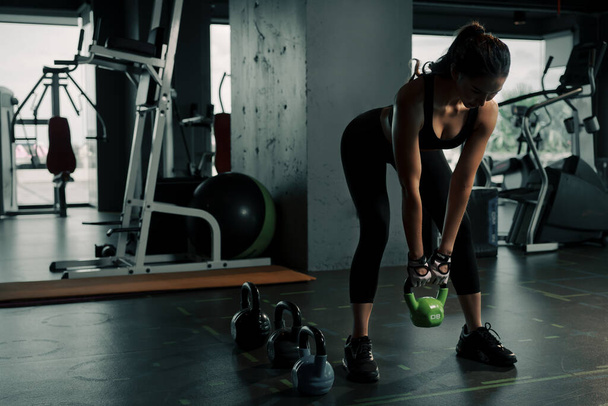Young woman lifts single kettlebell in upper arm exercise to build muscle. - Foto, imagen