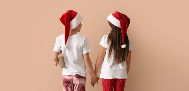 Cute children in pajamas and Santa hats holding hands on beige background - Foto, afbeelding
