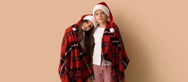 Roztomilé děti v pyžamu a Santa klobouky zabalené v kostkované na béžovém pozadí - Fotografie, Obrázek