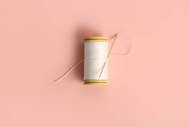 Thread spool with needle on pink background - Foto, afbeelding