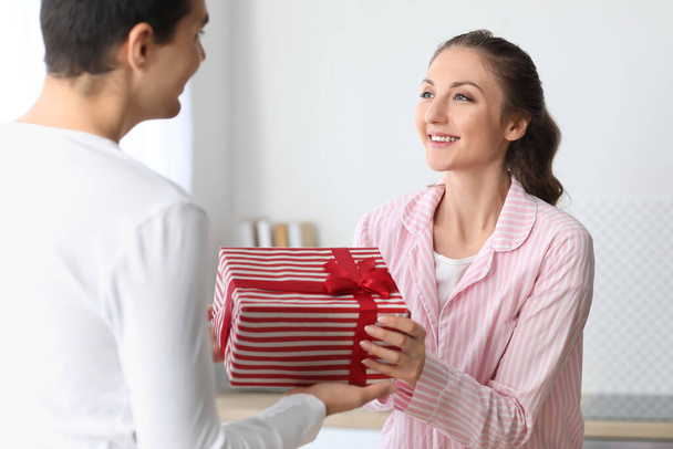 Young woman receiving gift from her beloved husband in kitchen on Christmas eve - Фото, изображение