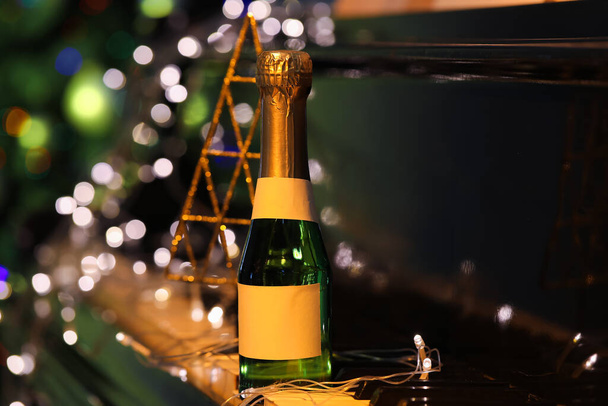 Láhev šampaňského a zářící vánoční světla na černém klavíru, detailní záběr - Fotografie, Obrázek