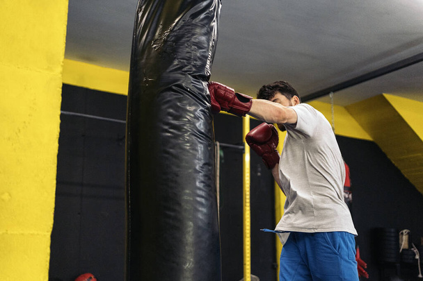 Unrecognizable kickboxing fighter performing punches on punching bag at the gym. Concept of kickboxing. - Foto, imagen