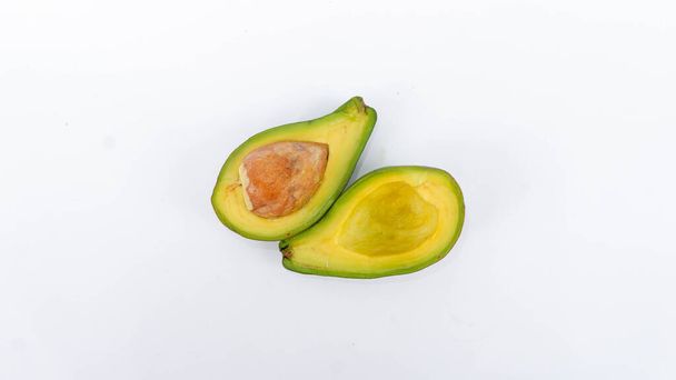 Grüne Avocadofrucht, die gespalten und reif ist. Enthält viele Vitamine für die menschliche Gesundheit. Auf einer weißen Matte platziert. - Foto, Bild