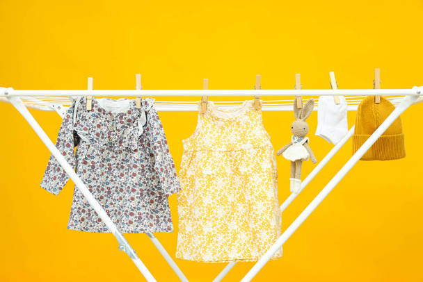 Roupas infantis e brinquedos pendurados e secados no rack de secagem no fundo amarelo - Foto, Imagem