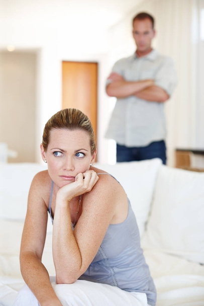 Problémy v ráji. žena sedí a vypadá rozrušeně, zatímco její manžel stojí v pozadí - Fotografie, Obrázek