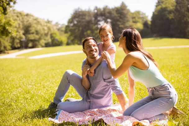 Счастливая молодая семья с милой маленькой дочкой развлекается в парке в солнечный день - Фото, изображение
