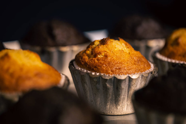 Freshly baked muffins in metal molds close-up in a bakery on a dark blurred background. - Photo, Image